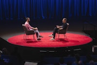 two men sitting on chairs in front of a stage